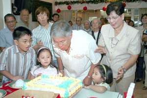The celebrator blows his cake as family and friends look on