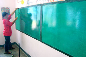 A volunteer repaints a blackboard inside a classroom