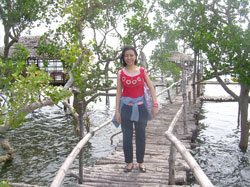 A visitor poses in a man-made bamboo bridge.  Behind her are cottages made of native materials