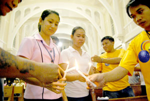 supporters and other members of the media light a candle during a holy mass at St. Clement's