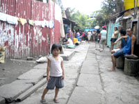 A child stares oblivious to the adults busily washing clothes in the “one for all” well or those who are playing “tong-its” behind her.