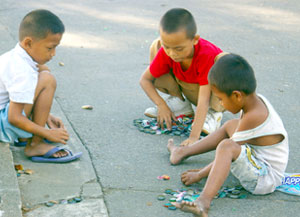 Three kids are playing 'tansan' (softdrink caps) one afternoon at Plaza Libertad.
